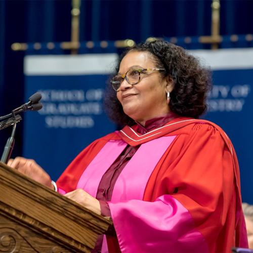 Lorna Goodison smiles while standing an a podium and wearing academic robes.