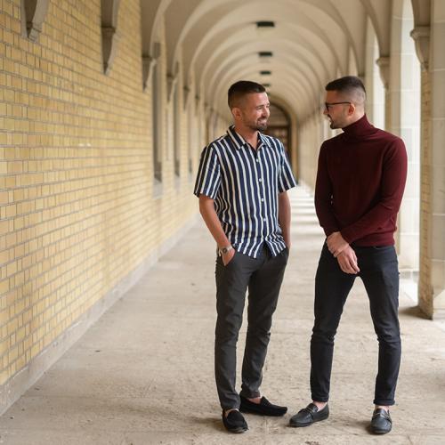 Patrick and Curtis Sobchak smile, facing each other, while standing in a covered walkway of golden stone.