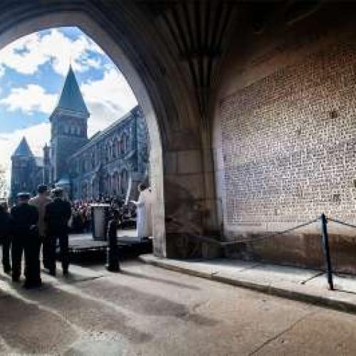 A group of people stand under a stone archway at the Soldiers' Tower with the blue sky shining behind them