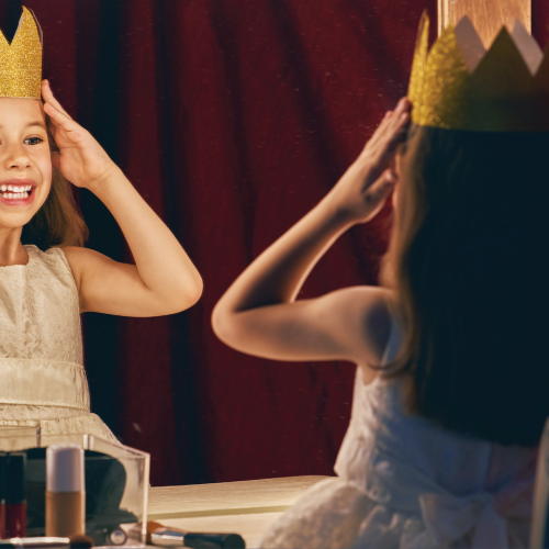 Little girl staring in the mirror putting on a crown