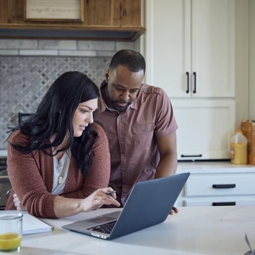 Couple reviews laptop screen together in a home setting.