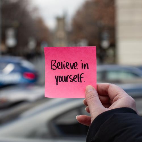Person holding sticky note that says "Believe in Yourself.