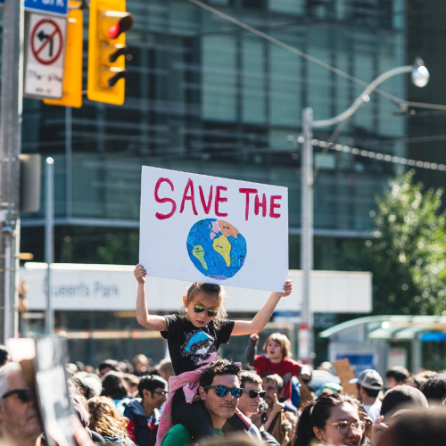 Child on parent's shoulder with poster which says Save the Planet. 