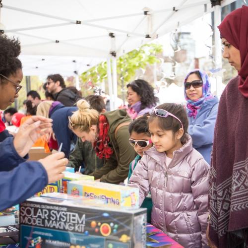 Image shows families visiting science exhibitions staffed by student volunteers.