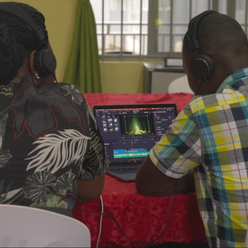 Two men wearing earphones edit a video on a laptop