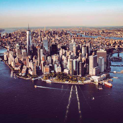 An aerial photo of Manhattan, New York City. You can see the iconic skyscrapers, the Hudson and East Rivers, and landmarks such as the One World Trade Center in the foreground and the Brooklyn and Manhattan Bridges in the distance.