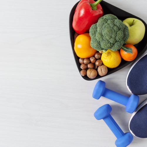 Image of navy sport shoes, blue light weights and a bowl of fruits and vegetables. 