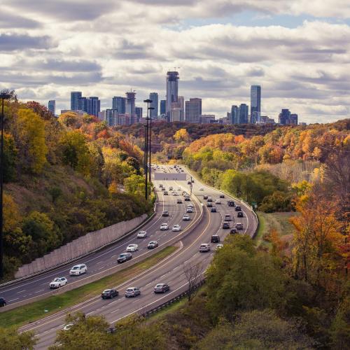 Image of highway during autumn with the sky line of  a city 