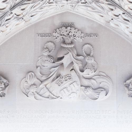 A close-up of the carved stone on the Soldiers' Tower memorial wall shows the U of T crest with tree, helmet, shield and knotted rope.