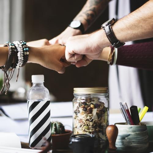 Several hands with varying skin tones fist-bump over a desk 