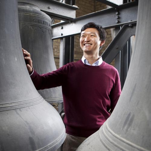 Carillonneur Roy Lee stands between giant bronze bells, smiling. (Image by Michelle Yee Photography.)