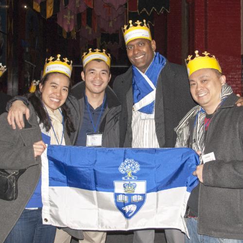 4 alumni standing together smiling holding a uoft flag