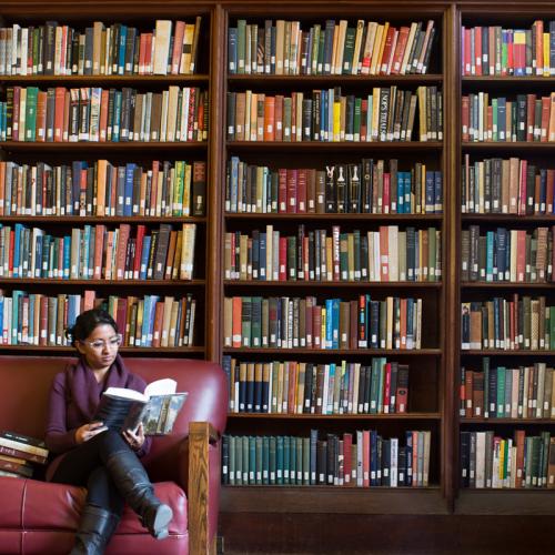 female alumni reading in the library surrounded by books