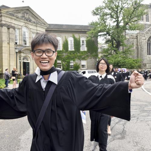 U of T grad in robes with arms outstretched in happiness, grinning at camera